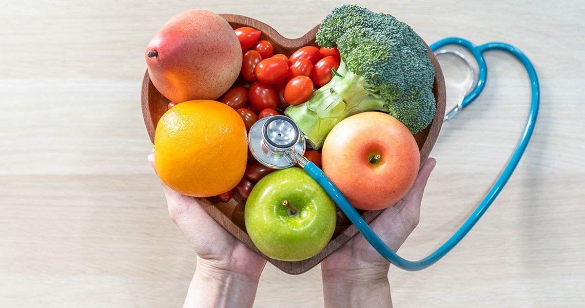 Fruits and vegetables, along with a stethoscope, fill a heart-shaped bowl
